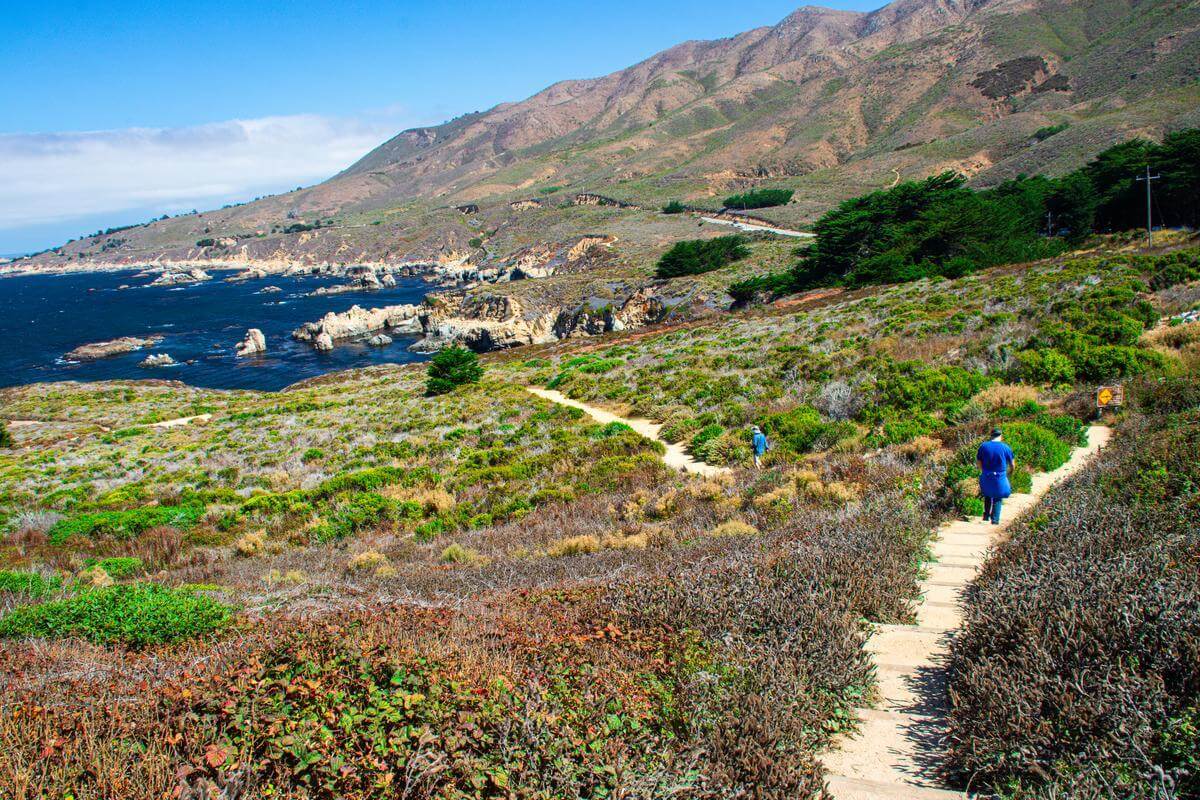 Solo Travel Guide to Monterey County Two people hiking separately on a trail at Garrapata State park. The mountains can be seen in the background, as well as the ocean
