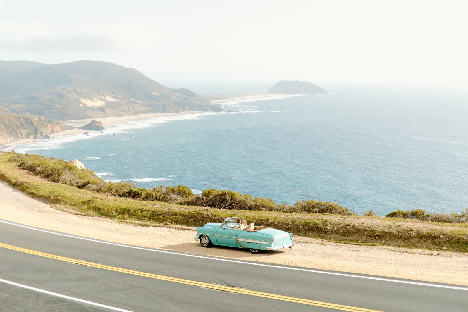 Team Building Activities in Monterey County This is an image of a blue classic car pulled over in a car turn out on Highway 1 with the Big Sur coastline in the background