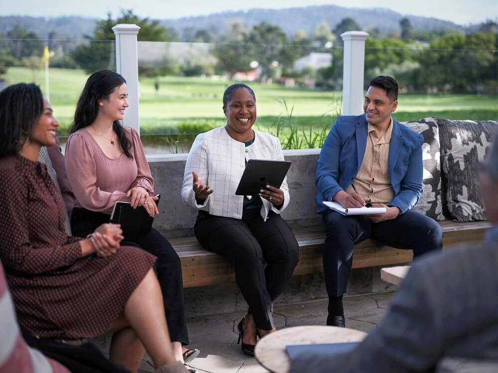 Group of people sat in an outdoor meeting space at Hyatt Regency Monterey with golf course behind them