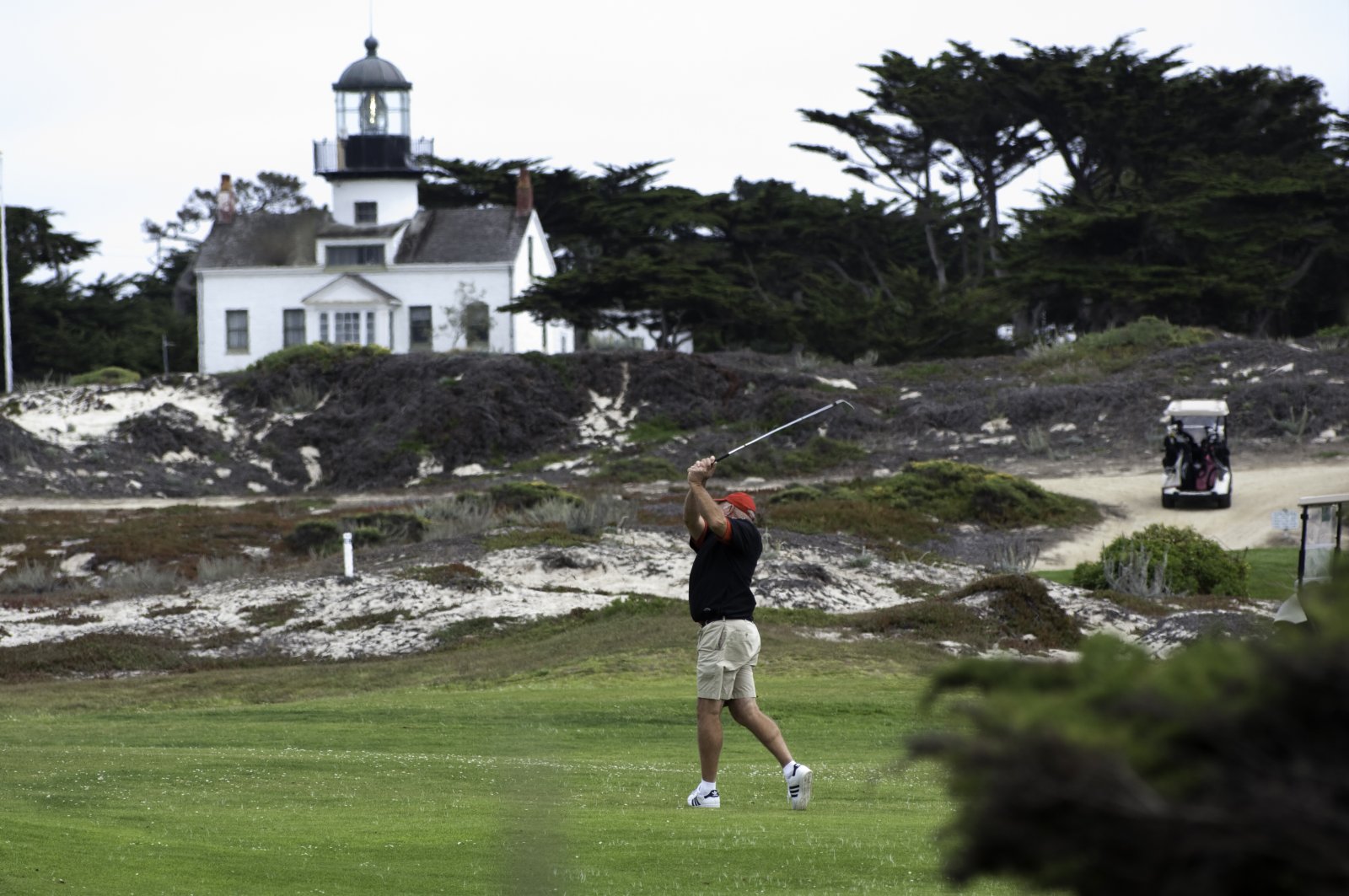 48 Hours in Pacific Grove This image is of a man hitting a golf ball with the lighthouse behind
