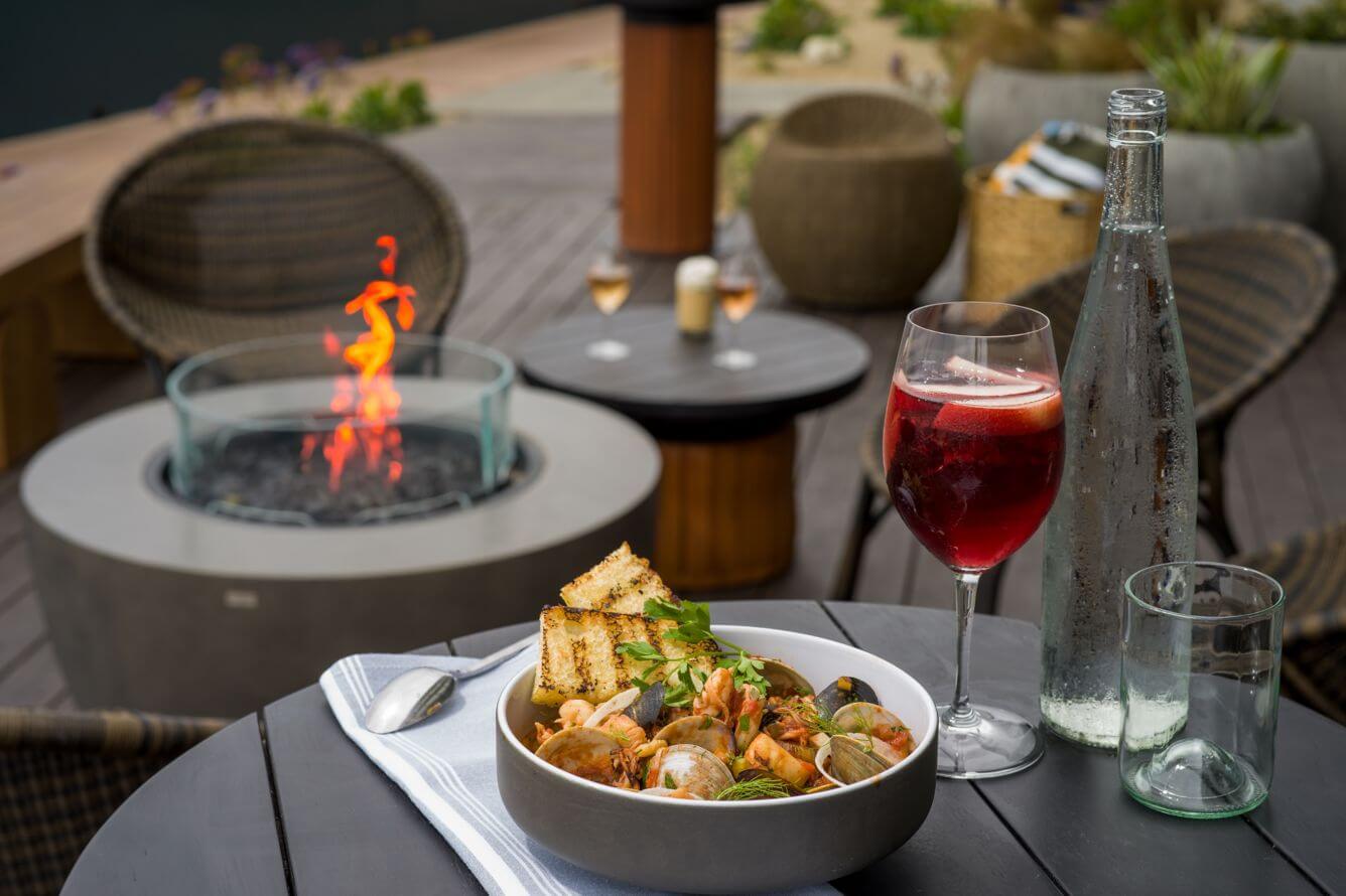 What's New Summer 2025 Dishes and wine next to a fireplace at Tidewater Restaurant at Monterey Beach Hotel
